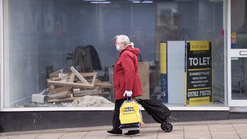 A woman wearing a mask walks past an empty shop which is To Let in Burslam last year