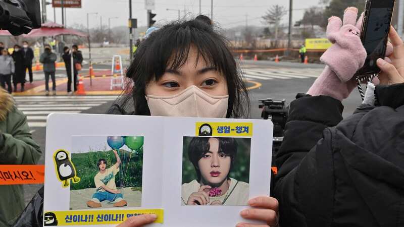 A fan holds a placard with a picture of BTS singer Jin in front of a military training unit in Yeoncheon, Korea (Image: AFP via Getty Images)