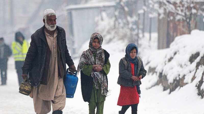 A man carrying gas canisters walks next to children along a street during snow fall in Kabul (Image: AFP via Getty Images)