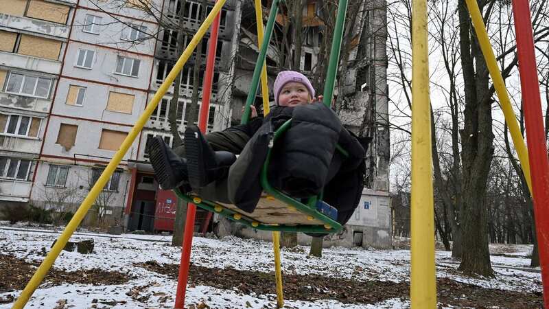 A child sits in a swing in front of an apartment block partially destroyed by shelling, in the Ukrainian city of Kharkiv (Image: AFP via Getty Images)