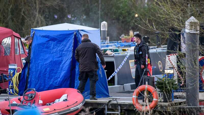 Police stand guard next to a forensic tent by a houseboat at the scene following the discovery of a woman