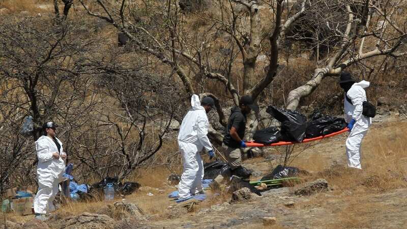 Forensic experts carry away several bags of human remains after they were extracted from the bottom of a ravine with a helicopter (Image: AFP via Getty Images)