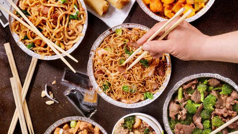 A group of people dig into a table full of Chinese noodle dishes. (Image: Getty Images)