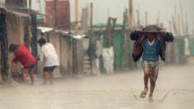 A child shields himself from torrential rains with his jacket as he runs through flooding caused by the meteorological phenomenon El Nino in 1998 (Image: AFP via Getty Images)