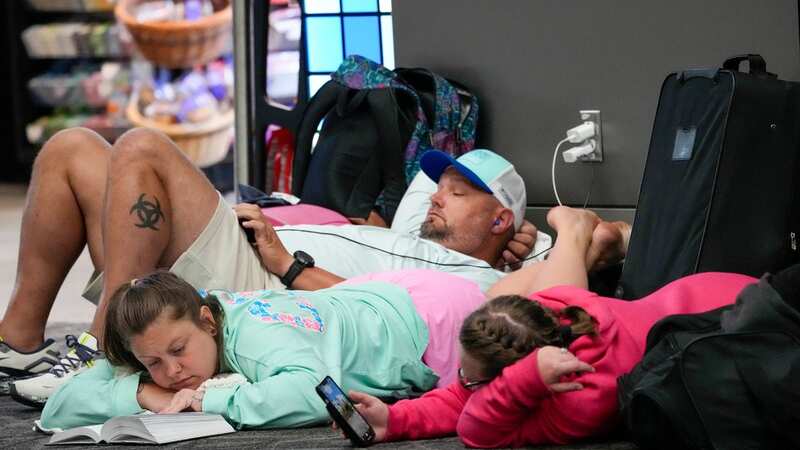 Travelers use their electronic devices while lying on the floor of the departures area of Terminal B at LaGuardia Airport (Image: AP)