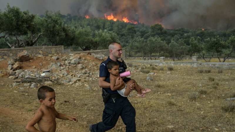 A Greek policeman evacuates a child from wild fire at the village of Agios Charamlabos, near the capital Athens (Image: AFP via Getty Images)