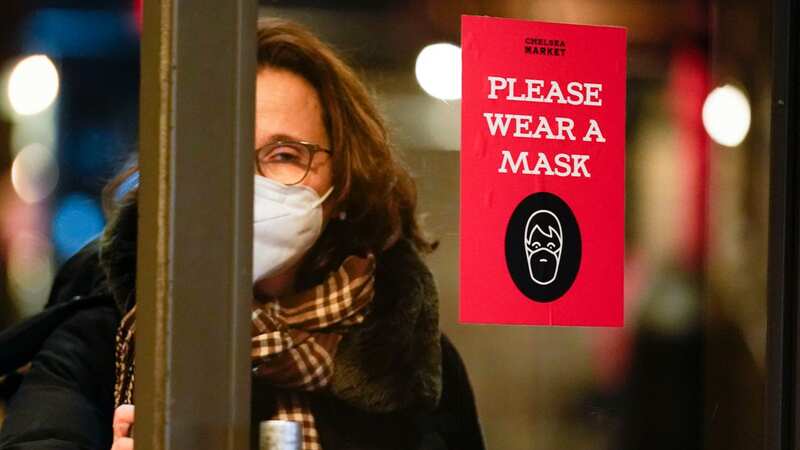 A woman walks through a door with a sign asking shoppers to wear masks, in New York, Feb. 9, 2022. (Image: AP)