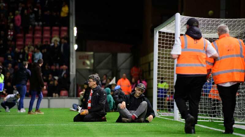 Fans resorted to sitting on the pitch to ensure that the game was stopped (Image: CameraSport via Getty Images)