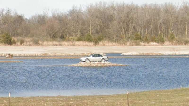 The modest silver saloon is perched on rocks in the middle of a lake (Image: Jam Press)