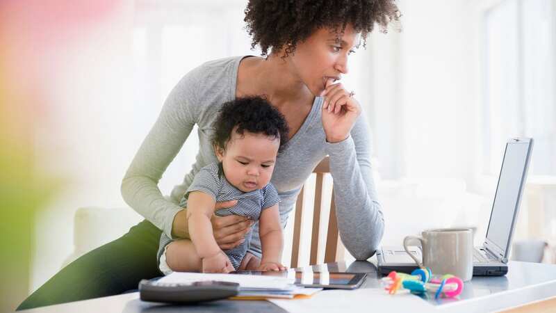Mother holding baby son worrying about finances on her laptop (Image: Getty Images/Tetra images RF)