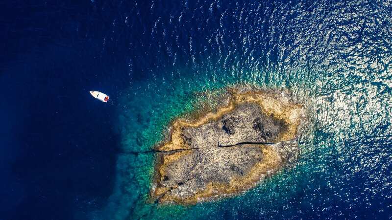 Aerial top view of a deserted island with white boat. Rocky shore of Zannone island near Ponza, Italy. Blue clear water on sunny day. 02