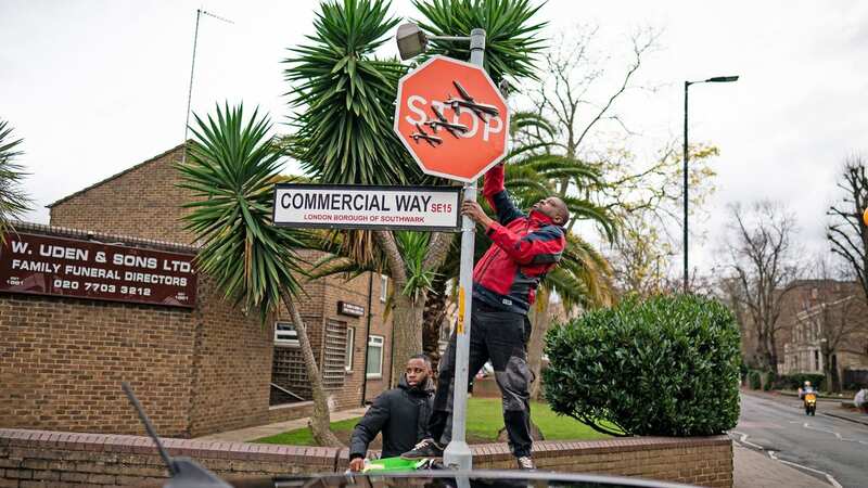 A person removes a piece of art work by Banksy, which shows what looks like three drones on a traffic stop sign (Image: PA)
