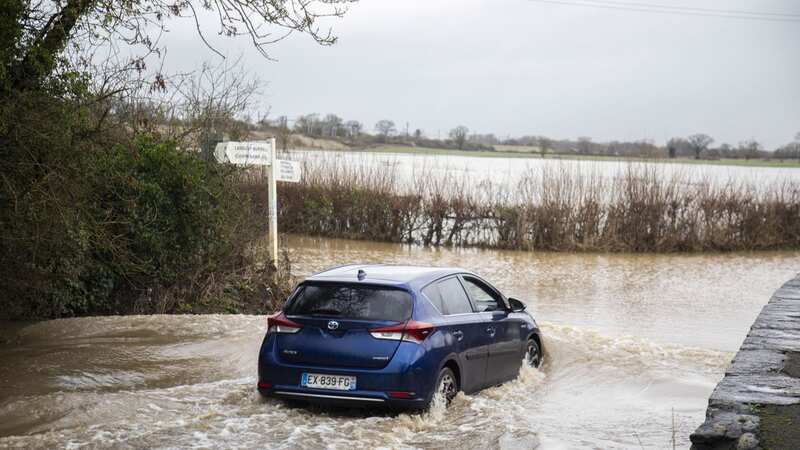A car drives through a flooded road in Wiltshire as heavy rain and winds batter the UK with more weather warnings issued (Image: Tom Wren SWNS)