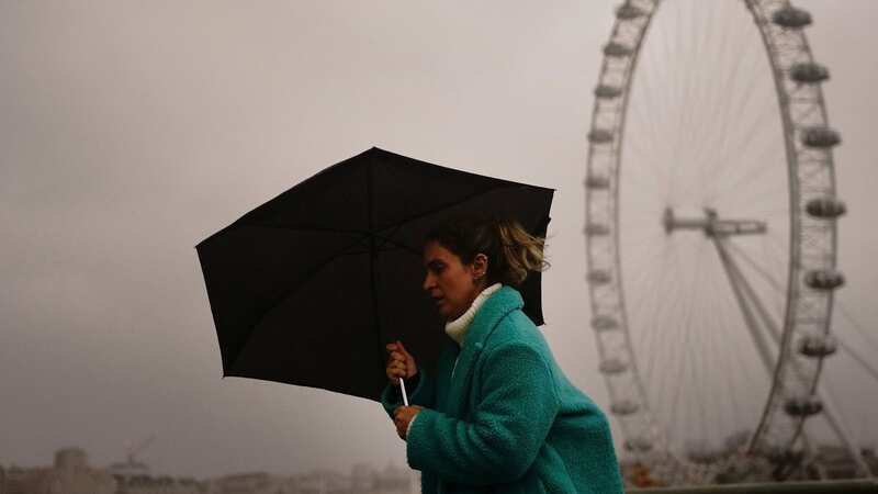 A woman covers up against the wet and windy weather in the capital (Image: PA)