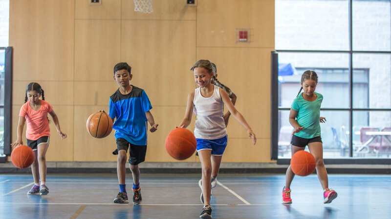 A multi-ethnic group of elementary age children are dribbling basketballs down the court in the gym. (Image: FatCamera/Getty Images)