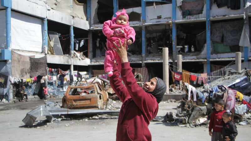 A Palestinian mother holds up her child at a UN school acting as refuge in Gaza (Image: Anadolu via Getty Images)