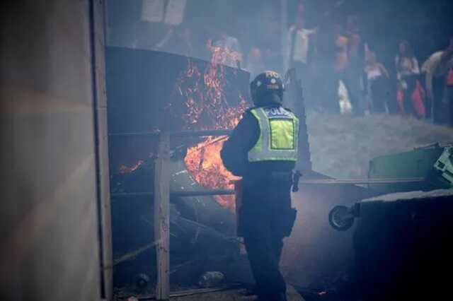 A police officer attempts to extinguish a wheelie bin that has been set alight by anti-migration protesters outside of the Holiday Inn Express in Manvers, which is being used as an asylum hotel, on August 4, 2024 in Rotherham ( Image: Getty Images)