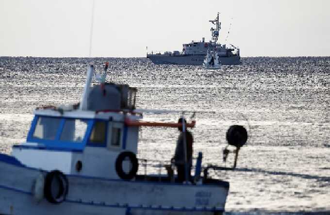 A fishing boat sails past a police vessel and a coastguard vessel off the coast of Porticello on Tuesday morning. Photograph: Guglielmo Mangiapane/Reuters