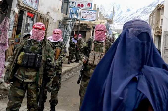 Taliban security personnel stand guard as an Afghan woman walks along a street at a market (Picture: AFP)