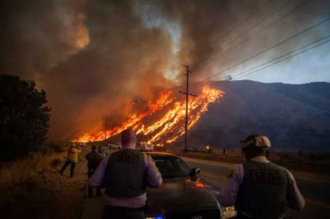 Police officers watch as flames race up the hill in the neighbourhood just northwest of Los Angeles ( Image: AFP via Getty Images)