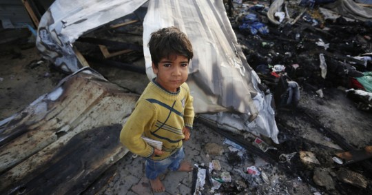 A child stood over smouldering remains of a tent in Gaza