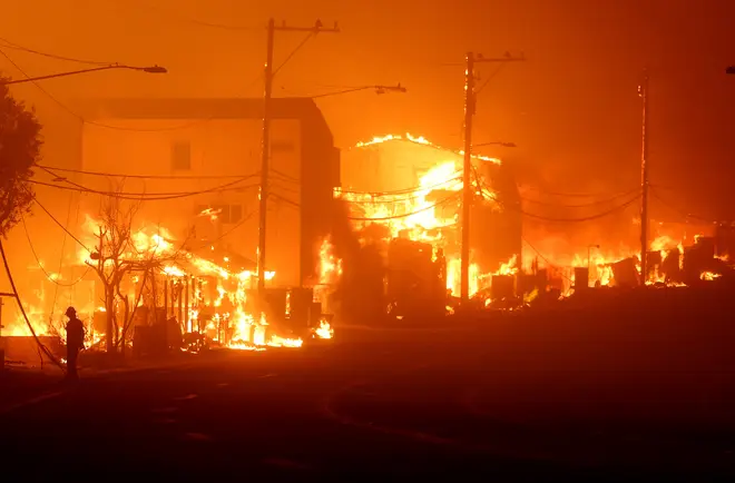 -A man stands along PCH as the Palisades Fire burns houses in Malibu Tuesday.