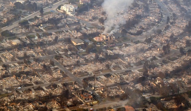 TOPSHOT - In this aerial view taken from a helicopter, homes burned from the Palisade fire smolder near the Pacific Palisades neighborhood of Los Angeles, California on January 9, 2025. Massive wildfires that engulfed whole neighborhoods and displaced thousands in Los Angeles remained totally uncontained January 9, 2025, authorities said, as US National Guard soldiers readied to hit the streets to help quell disorder. Swaths of the United States’ second-largest city lay in ruins, with smoke blanketing the sky and an acrid smell pervading almost every building. (Photo by JOSH EDELSON / AFP) (Photo by JOSH EDELSON/AFP via Getty Images)