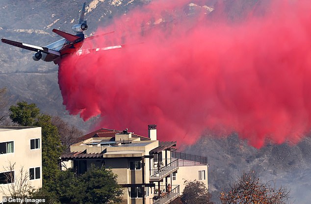 A person watches from a balcony as a firefighting aircraft drops the fire retardant Phos-Chek near homes during the Palisades Fire