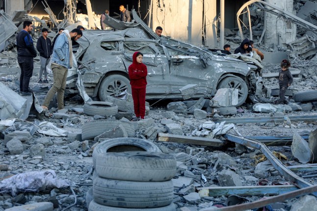 Men and children stand next to a destroyed car amidst debris and rubble by a collapsed building at the site of Israeli bombardment on a residential block in Jalaa Street in Gaza City on January 14, 2025 amid the ongoing war in the Palestinian territory between Israel and Hamas. (Photo by Omar AL-QATTAA / AFP) (Photo by OMAR AL-QATTAA/AFP via Getty Images)