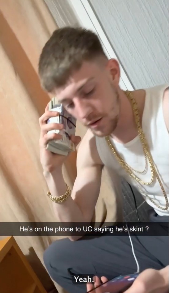 A man wearing gold chains holds a stack of cash to his ear while speaking on the phone, claiming to be struggling financially. qhiddeidehiehinv