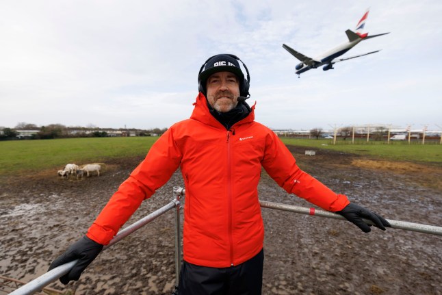 Jerry Dyer, the founder and creator of Big Jet TV flight and plane landing YouTube live streaming channel looking at the camera with a British Airways plane behind him approaching to land at Heathrow Airport.