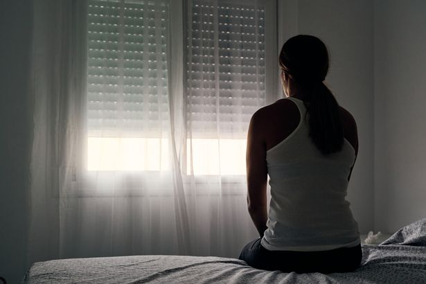 Stock image of a woman sitting on her bed and looking out the window