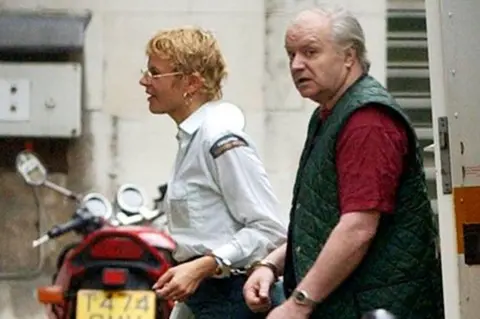 PA Media Tony Martin is seen with a prison guard in a blurry photo. She is wearing a white shirt and Martin has on a red T-shirt and a green jacket