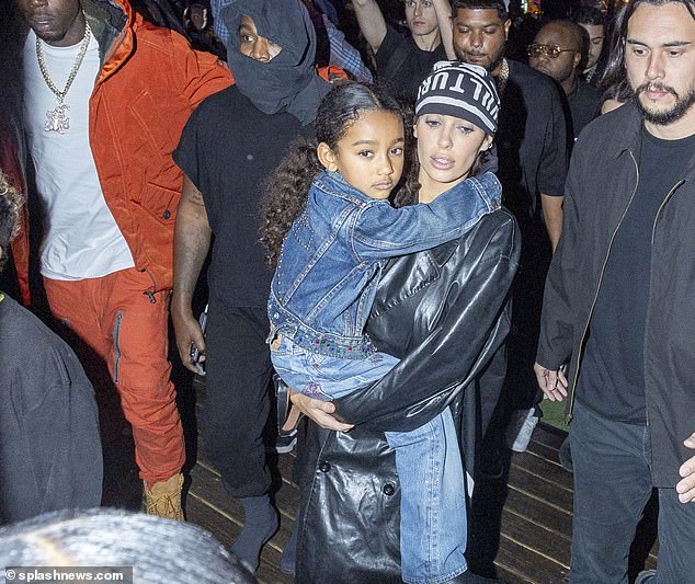 Last year Censori shocked many in Paris when she appeared during fashion week wearing a fur bolero jacket, black stilettos and a pair of ultra-sheer tights, but no underwear (pictured holding Kanye and Kim’s daughter Chicago)