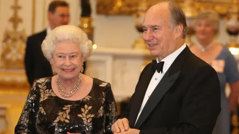 PA Media Queen Elizabeth II wearing a black dress with golden leaf patterns standing next to the Aga Khan wearing a black tuxedo qhidqhideziqkzinv