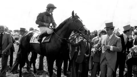 PA Media File photo dated 03/06/81 of Shergar during the lead in by owner Aga Khan (top hat) with jockey Walter Swinburn after winning the Derby Stakes Classic at Epsom. 