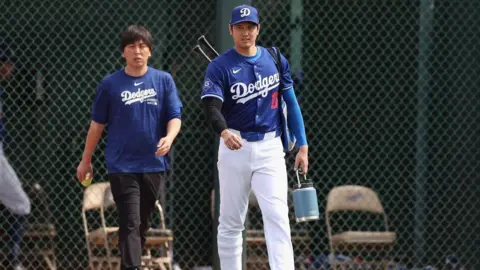 Getty Images Ippei Mizuhara, the former interpreter to Los Angeles Dodgers’s Shohei Ohtani, seen walking with the baseball star on the field. He is wearing a blue Dodgers shirt and Shohei is in his baseball uniform.  qhiqqxiuziqtzinv