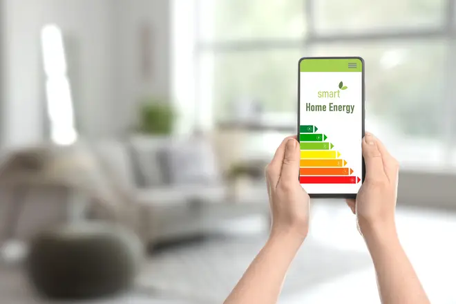 Hands holding mobile phone with energy efficiency rating on screen in room