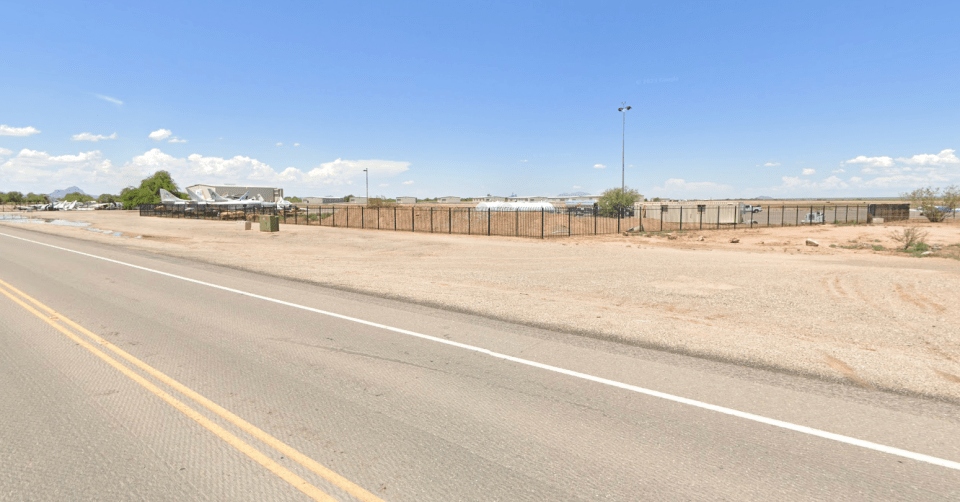 Roadside view of a fenced-in area with several airplanes.