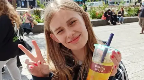 Family handout Rhianan Rudd holding up a bubble tea and giving a peace sign to the camera qhidqxitkikeinv