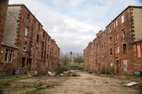 Sandstone fronted tenements. The windows are smashed and rubble is piled up in the street.  qhxidiqxkiqxqinv
