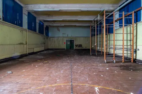 Urbandoned A school gym hall. Climbing bars are on the right of the picture. The paint on the walls is peeling