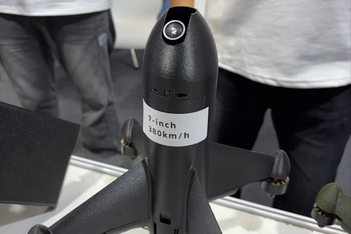 A black, 3D-printed interceptor drone labeled "7-inch 380km/h" with a camera at its nose is displayed on a table. qhxidiqxkiqruinv